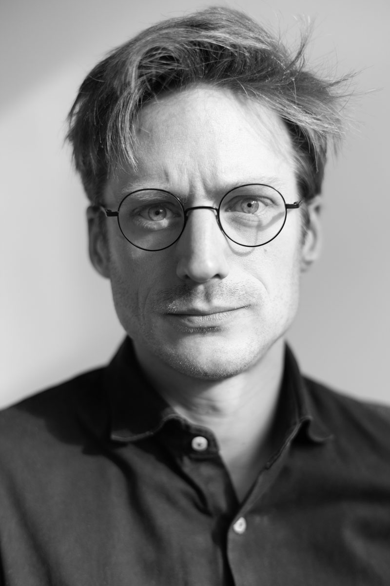 Black-and-white portrait of a man with round glasses and tousled hair, in a shirt.