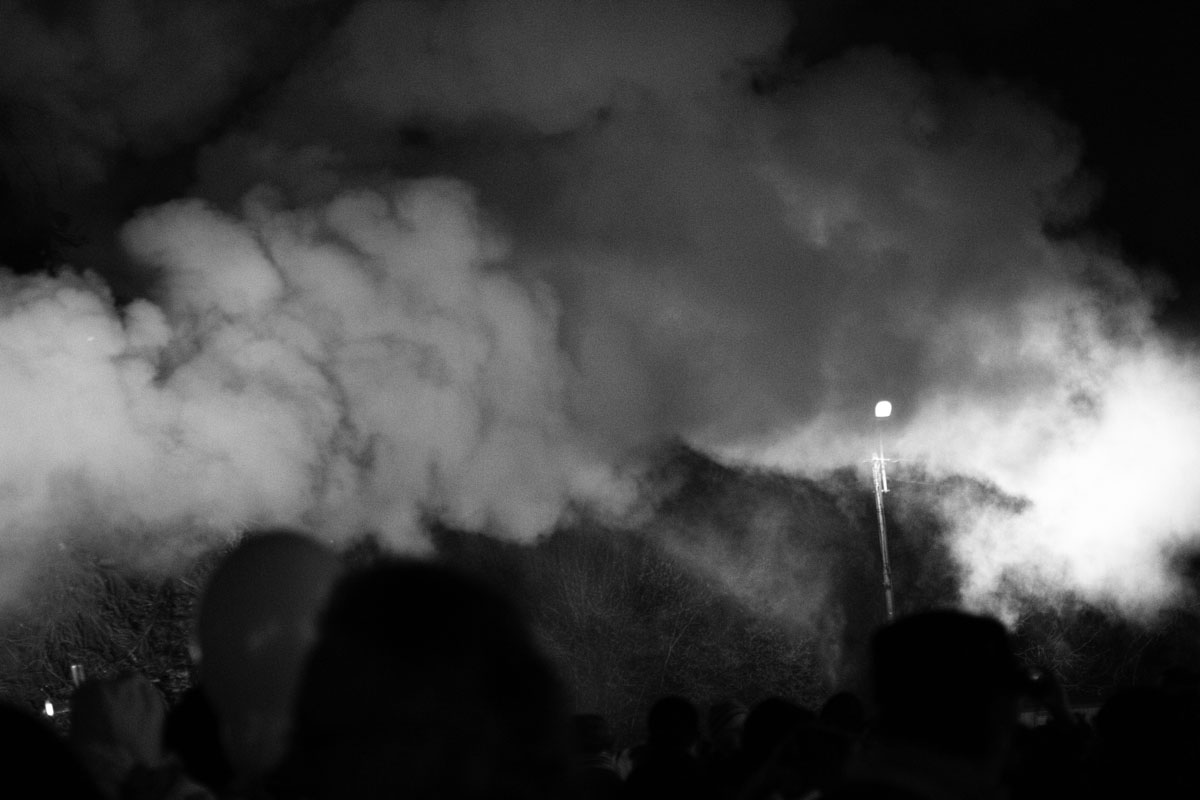 Dense smoke over a silhouetted crowd at night.
