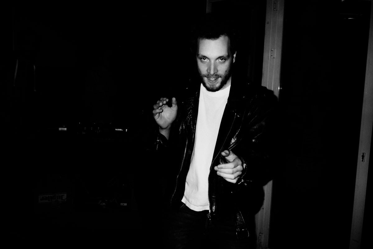 A man in a leather jacket emerges from the dark.