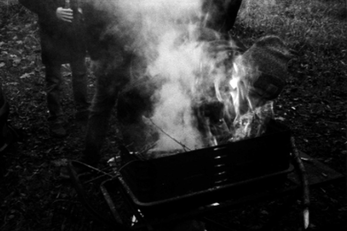 A man blows into a barbecue; the flames and smoke engulf his head.