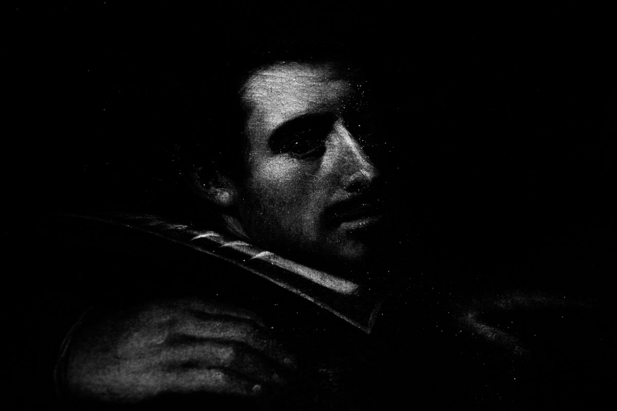 An old painted portrait of a man in a ruff, his face emerging from the dark.
